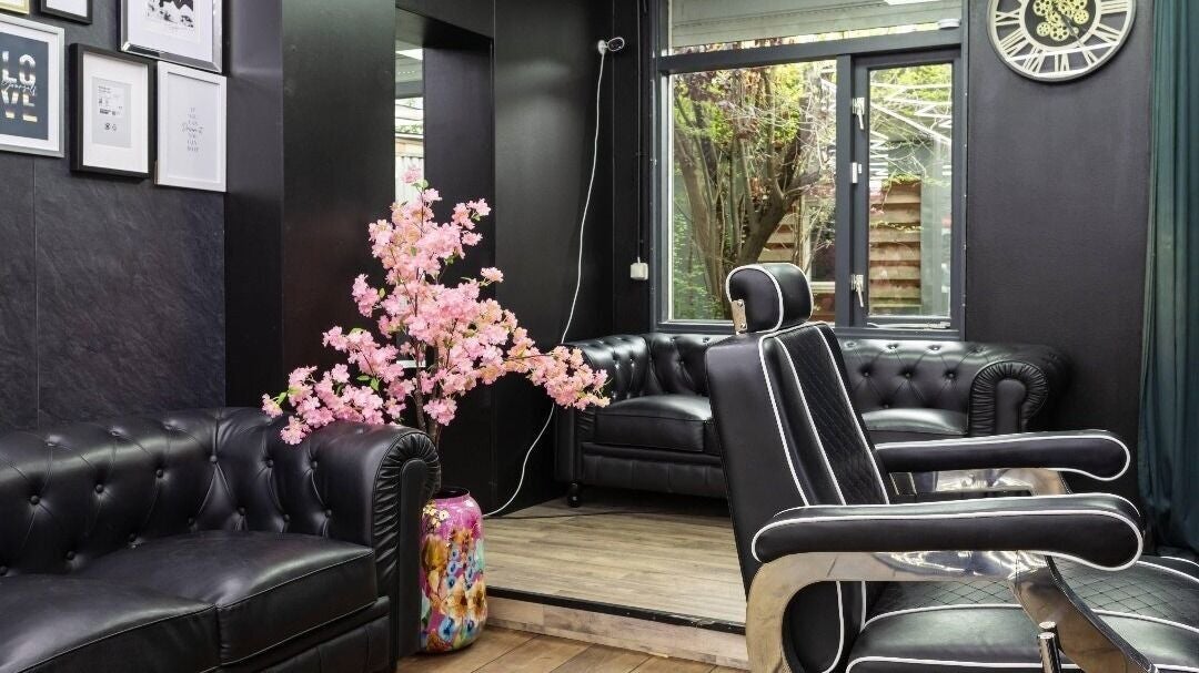 Een hoek met een chesterfield bank, een roze bloesem in een bonte vaas en een ronde klok