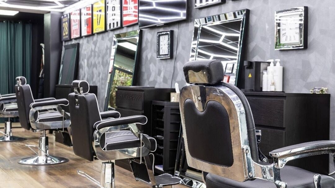 Een rij barberstoelen en spiegels langs de grijze muur met ingelijste shirts
